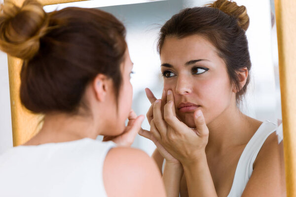 Portrait of beautiful young woman removing pimple from her face in a bathroom home.