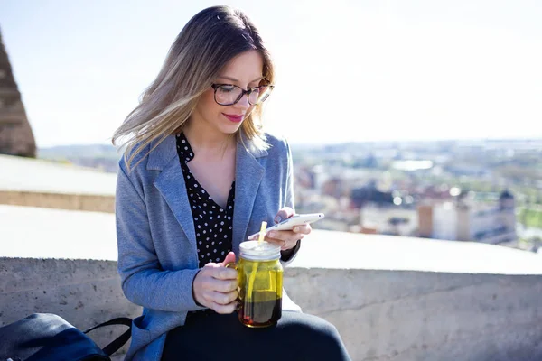かなり若い女性が通りでジュースを飲みながら彼女の携帯電話を使用してのショット — ストック写真