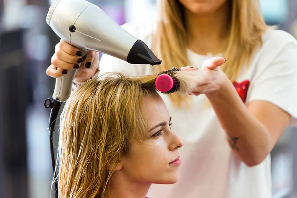 Shot of hairdresser drying female customer's hair in beauty salon.