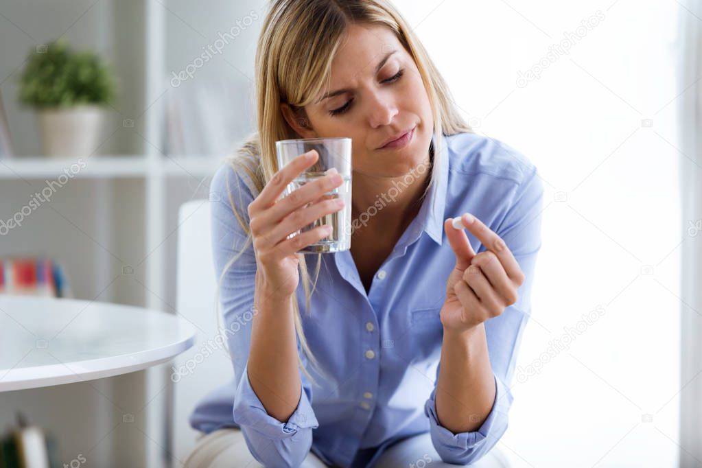 Shot of depressed young woman taking pills at home.