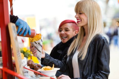 Atış iki güzel genç kadın bir gıda kamyon park Barbekü patates satın alma.