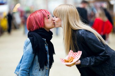 Shot of beautiful young women kissing on the street. clipart