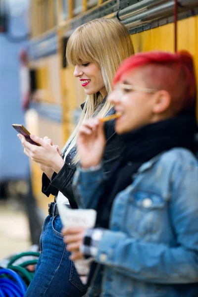 Фотография Красивой Молодой Женщины Использующей Мобильный Телефон Пока Подруга Ест — стоковое фото