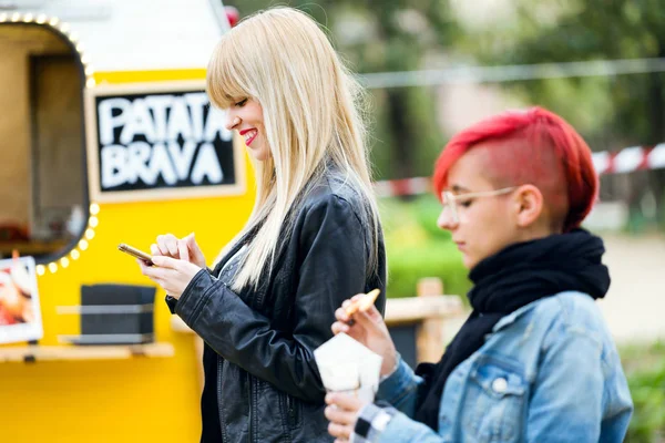 かなり若い女性の携帯電話を使用してのショットながら通りにジャガイモを食べる彼女の友人 — ストック写真