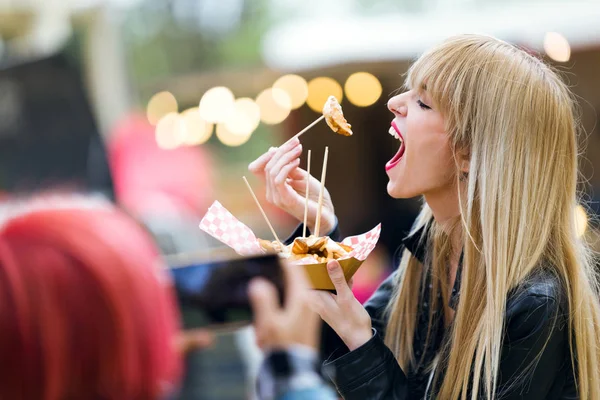 ジャガイモを食べて美しい若い女性のショット中通りで写真を撮って 彼女の友人 — ストック写真