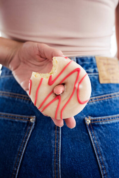 Крупный план молодой красивой женщины, прячущей пончик у себя за спиной
.