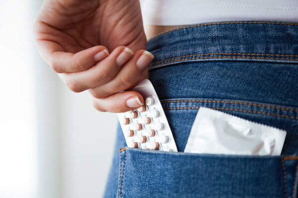 Close-up of woman with contraceptive pills and condom in the pocket of blue jeans.