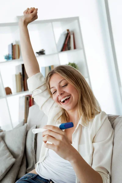 自宅のソファーに肯定的な結果で妊娠テストを見て幸せな若い女のショット — ストック写真