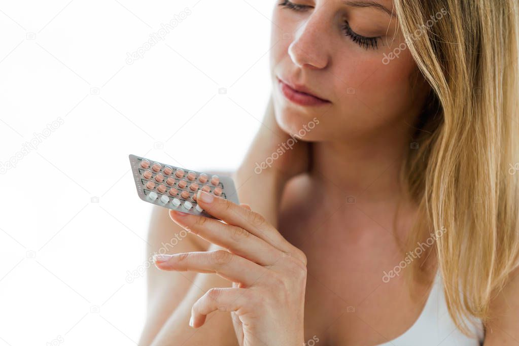 Shot of beautiful young woman holding contraceptive pills over white background.