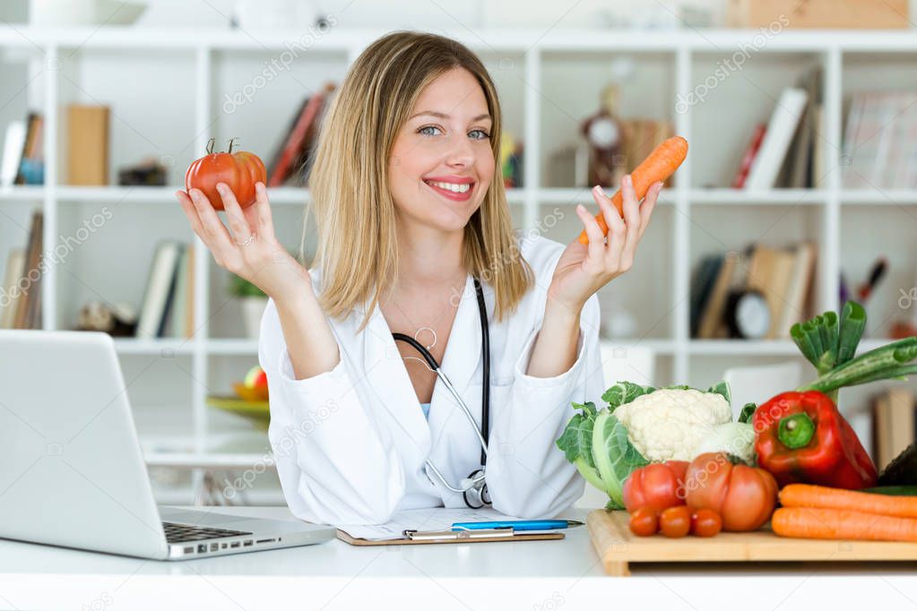 Portrait of beautiful young nutritionist looking at camera and holding fresh vegetables in the consultation.