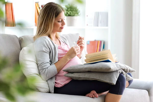 Foto Hermosa Mujer Embarazada Leyendo Libro Comiendo Yogur Sofá Casa — Foto de Stock