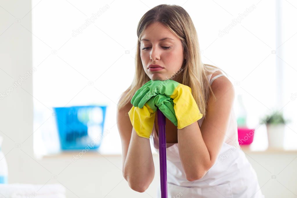 Portrait of boring young woman holding broom while cleaning at home.