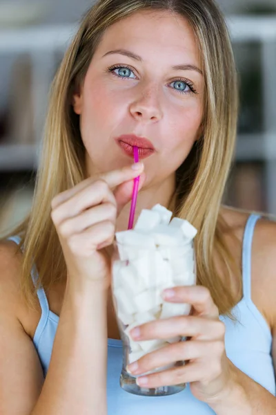 Mooie jonge vrouw camera kijken terwijl simuleren om te drinken van suiker in een glas kopje thuis. — Stockfoto