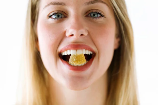 白い背景の上のカメラを見て口の中で甘いお菓子と美しい若い女性. — ストック写真