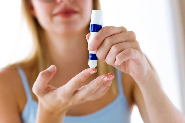 Jovem mulher picando-se para obter uma amostra de sangue e realizar um teste de glicose . — Fotografia de Stock