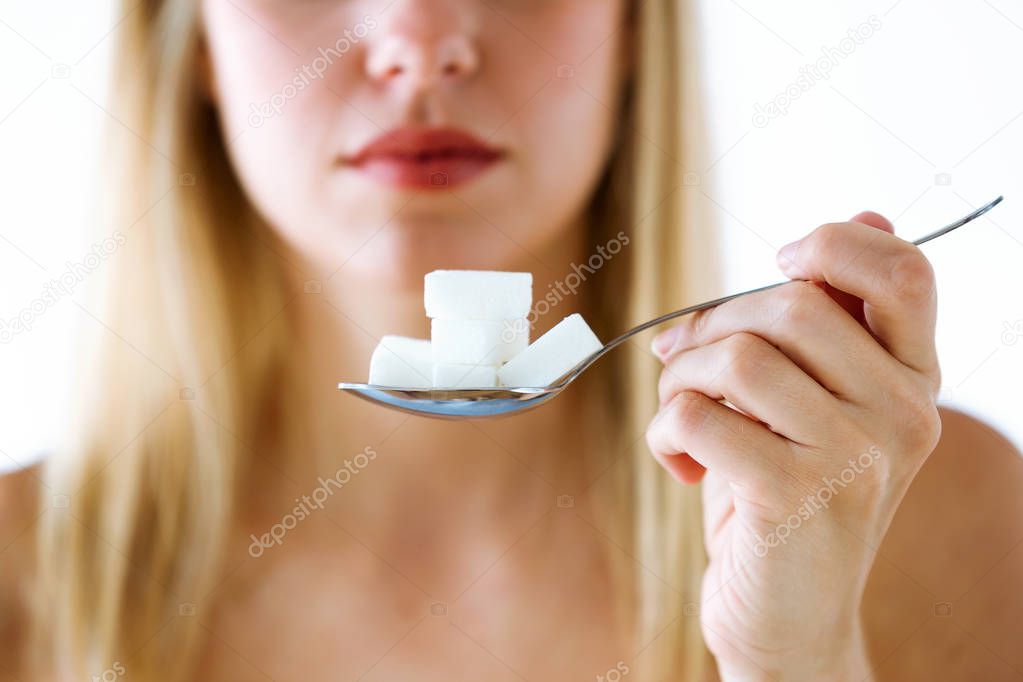 Beautiful young woman holding spoon with white sugar cubes over white background.