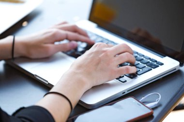 Laptop ile telefon pil bir kafede yüklenirken çalışan genç kadın.