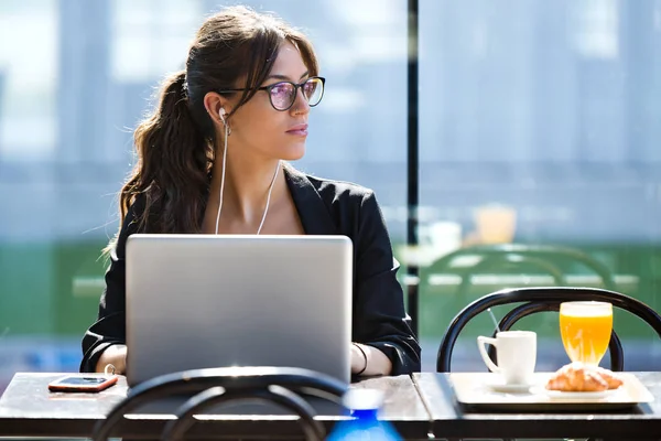Красивая молодая женщина смотрит в сторону, работая с ноутбуком в кофейне . — стоковое фото