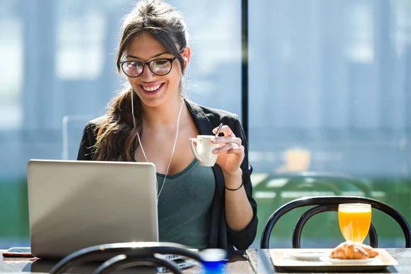 Mooie jonge vrouw drinken koffie tijdens het werken met haar laptop in een koffieshop. — Stockfoto