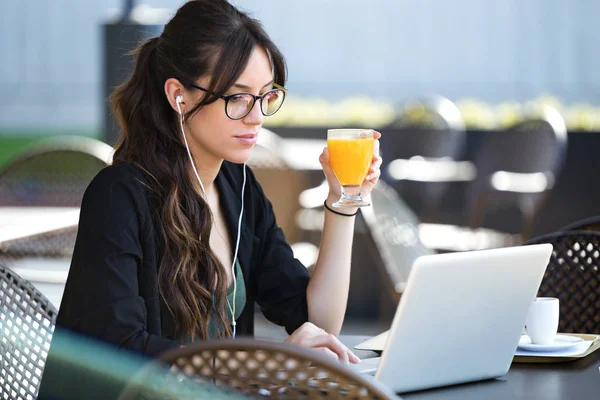 コーヒー ショップで彼女のラップトップで作業しながらオレンジ ジュースを飲んで美しい若い女性のショット — ストック写真
