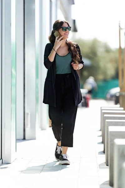 Hermosa joven empresaria hablando con su teléfono móvil mientras camina por la ciudad . — Foto de Stock