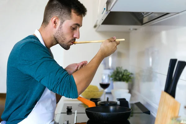 Portrait Handsome Young Man Tasting Fried Wooden Spoon Kitchen Home — Stock Photo, Image