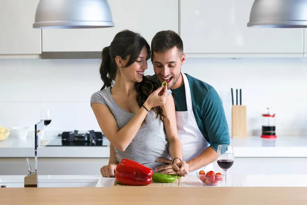 ピーマンと彼女の夫を餌と自宅の台所で笑顔の女性のロマンチックな瞬間を持っている美しいの若いカップルのショット — ストック写真