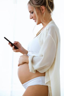 Güzel genç hamile kadın manifatura izole beyaz komutunuz onun smartphone ile çekim.