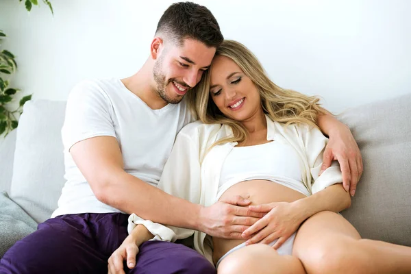 自宅のソファの上に横たわっている間美しい妊婦の腹に触れるハンサムな若い男のショット — ストック写真