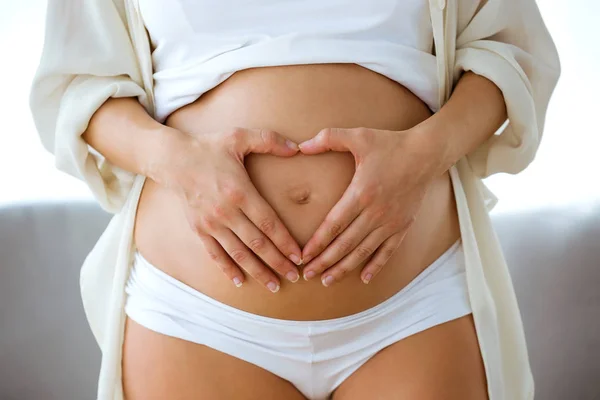 Close Jovem Grávida Tocando Barriga Com Coração Feito Dedos Casa — Fotografia de Stock