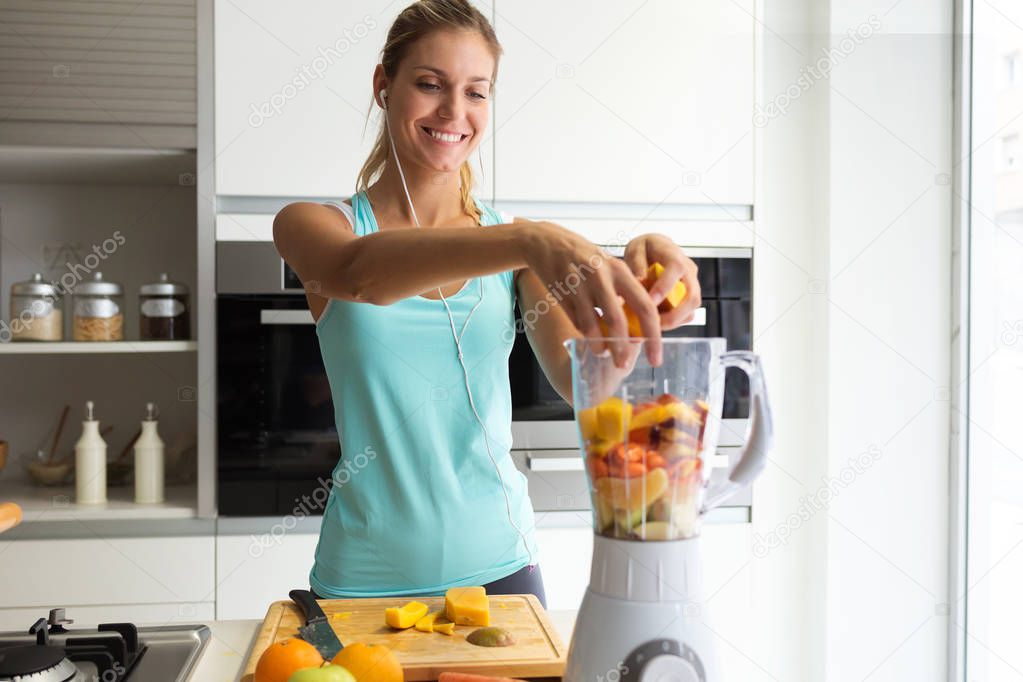 Shot of sporty young woman making a vegetable smoothie while listening to music in her kitchen.