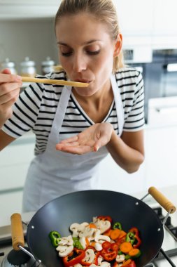 Yemek ve mutfak evde tahta kaşıkla yemek tatma sağlıklı genç kadının atış. 