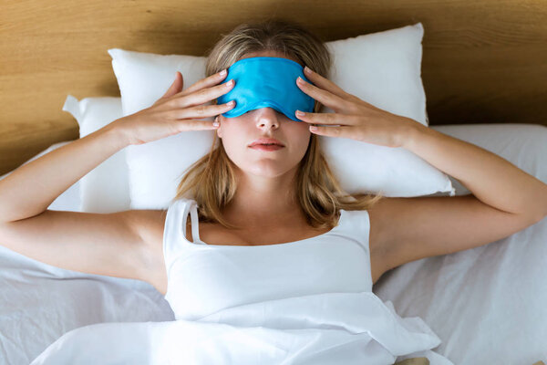 Shot of beautiful young tired woman trying to sleep with sleep mask resting on bed in bedroom at home.