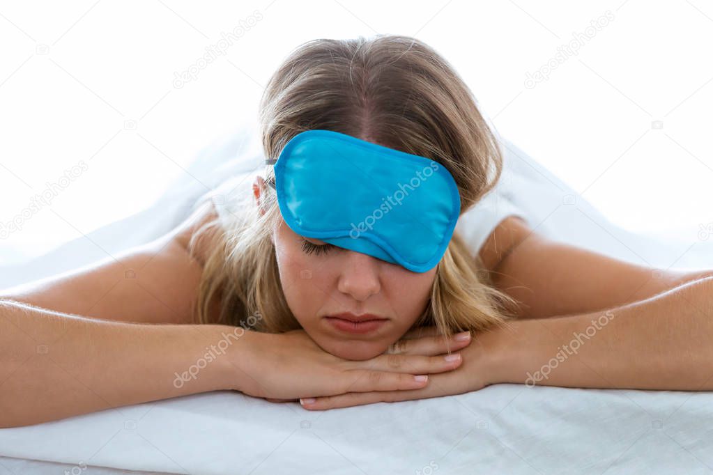 Shot of beautiful young exhausted woman with sleep mask suffering insomnia trying to sleep over white blackground.