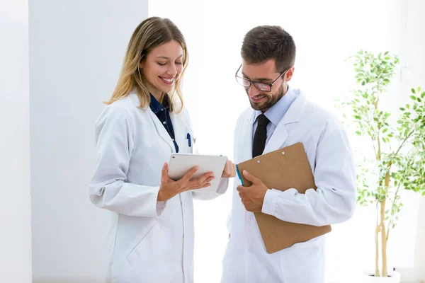 Usmívající se mladí lékaři vypadající lékařské zprávy v digitálním tabletu v ordinaci. — Stock fotografie