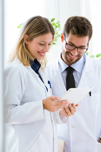 Giovani medici sorridenti in cerca di rapporti medici in tablet digitale nello studio medico . — Foto Stock