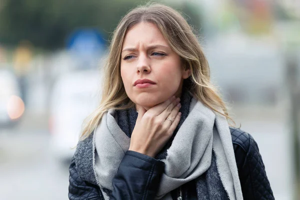 通りに歩いてひどい喉の痛みを持つ病気の若い女性のショット — ストック写真