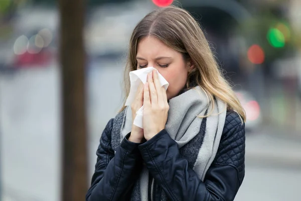 Shot of illness young woman sneezing in a tissue in the street.