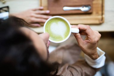 Yakın çekim Genç kadının kafedeki wodden masada Matcha yeşil çay kahve içme. Üstten görünüm.