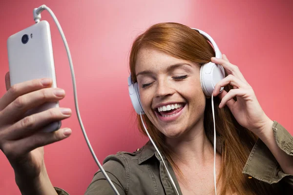 ピンクの背景の上にイヤホンで音楽を聴く笑顔美人のショット — ストック写真