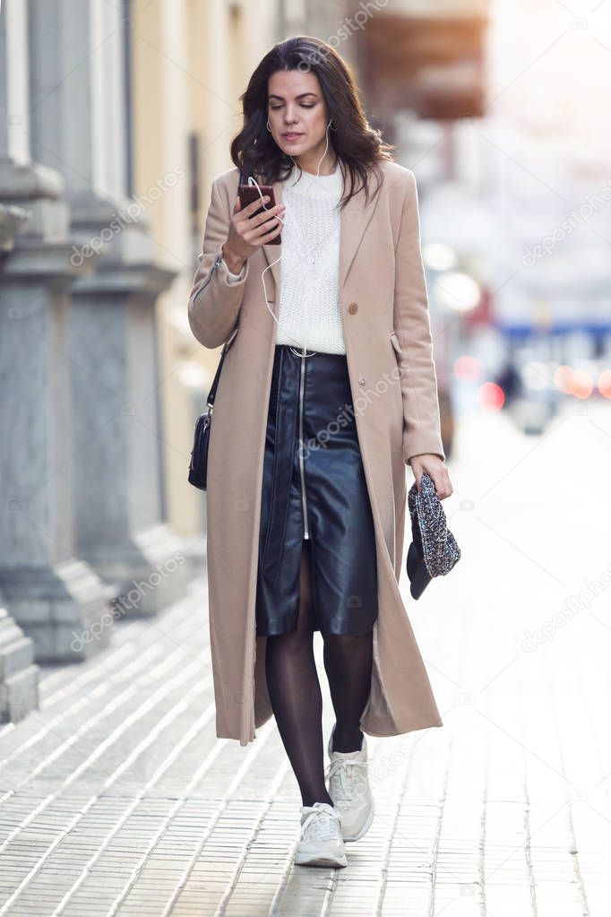 Shot of pretty young woman listening to music with her mobile phone while walking in the street.