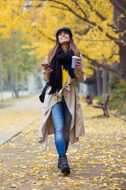 Gökyüzüne bakmak ve sonbahar sırasında parkta yürüme sırasında cep telefonu kullanan genç ve güzel kadın görüntüsünü.