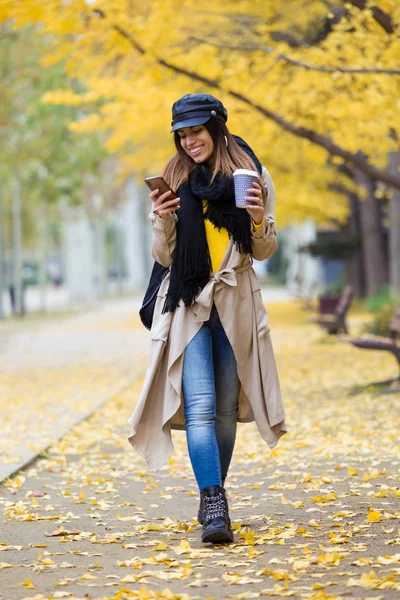 秋の間に公園を通って歩いている間彼女の携帯電話を使用してかなり若い女性のショット — ストック写真