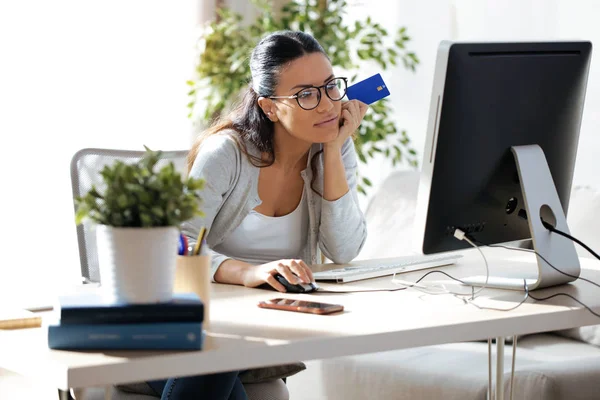自宅のコンピューターとオンライン ショッピングのための青のクレジット カードを保持しているかなり若い女性のショット — ストック写真