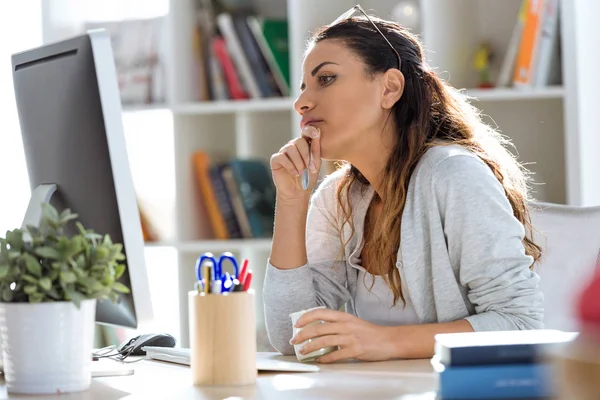 オフィスにあるコンピューターで作業しながらヨーグルトを食べてかなり若いビジネス女性のショット — ストック写真