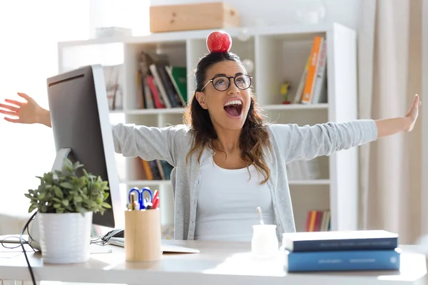 オフィスで彼女の頭の上に赤いリンゴを保持と楽しんで幸せな若いビジネスウーマンのショット — ストック写真