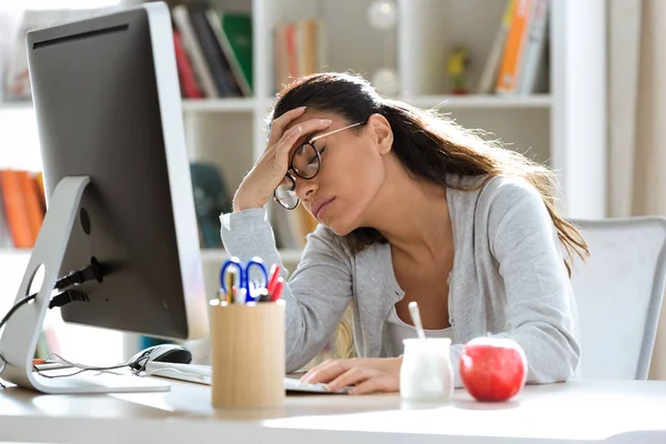 Mujer de negocios joven y cansada que tiene dolor de cabeza mientras trabaja con la computadora en la oficina . — Foto de Stock