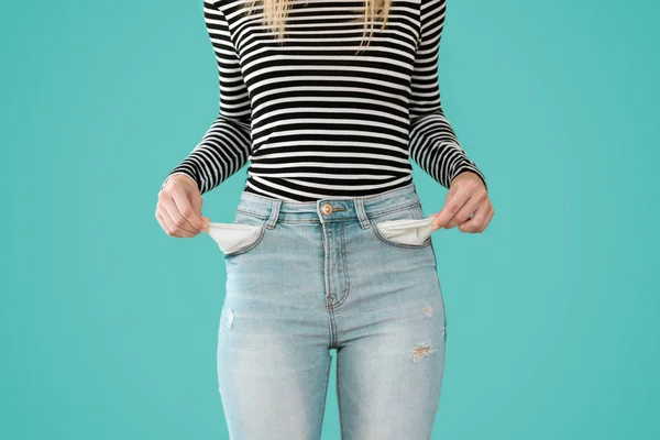 Jonge vrouw toont heeft niet niets in de zakken van haar jeans op blauwe achtergrond. — Stockfoto