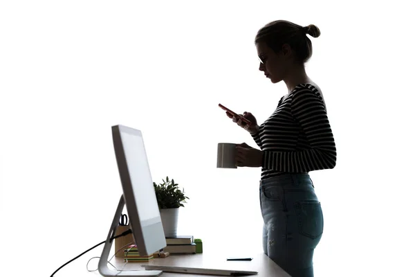 Красива молода жінка використовує свій мобільний телефон, стоячи перед комп'ютером на білому тлі . — стокове фото