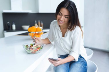 Genç ve güzel kadın mutfakta ev salatası yerken onu cep telefonuyla çekim.